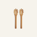 Two wooden pasta servers with decorative ends on a light beige background