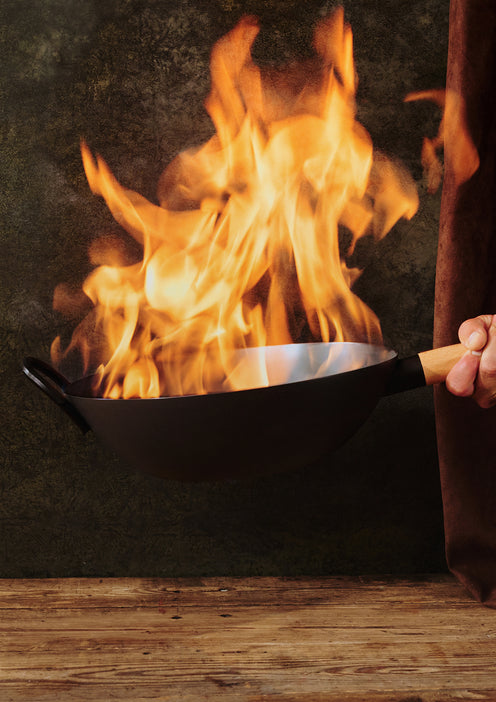 Person holding a black frying pan over a fire with flames