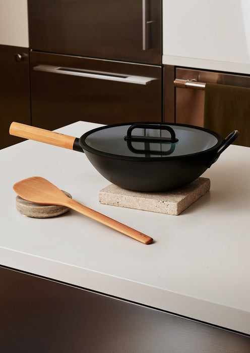 Black wok with wooden spatula on a kitchen counter