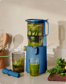 Blue juicer with green juice and vegetables on a kitchen counter
