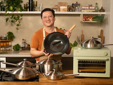 Man holding a black frying pan in a kitchen with various cookware and appliances.