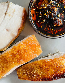 Slices of roasted pork belly with a side of dark sauce on a light surface
