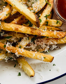 French fries with Parmesan cheese and herbs on a white plate with a side of ketchup.
