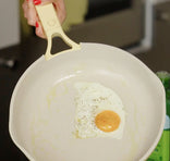 Fried egg in a yellow frying pan held by a hand with red nail polish.