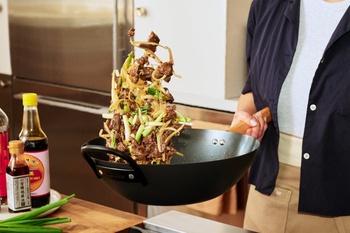A hand holding a wok tossing food inside