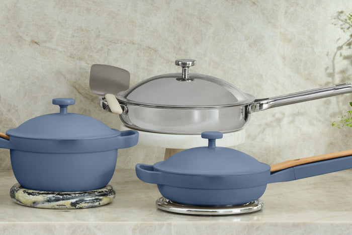 A blue pot, a stainless steel pan, and a blue pan on a marble countertop