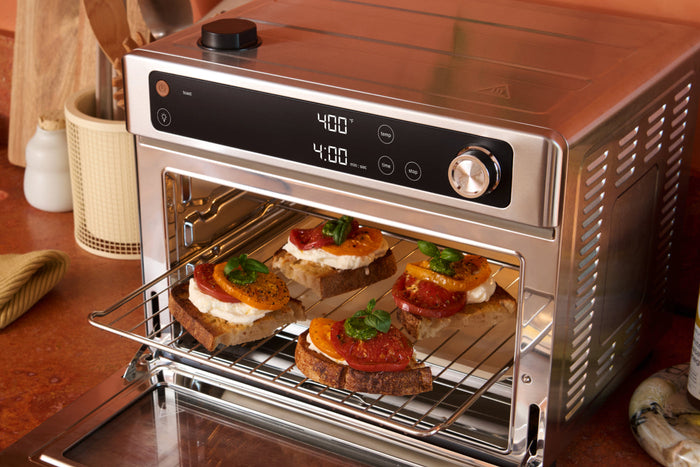 Pieces of toast cut in half with burrata cheese, slices of tomato, and basil on top in a counter top toaster oven