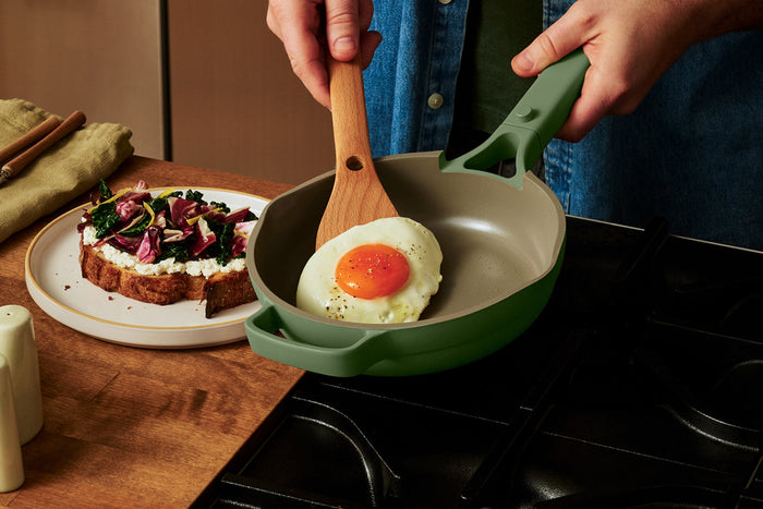 A hand holding a spatula taking out an egg from a green pan