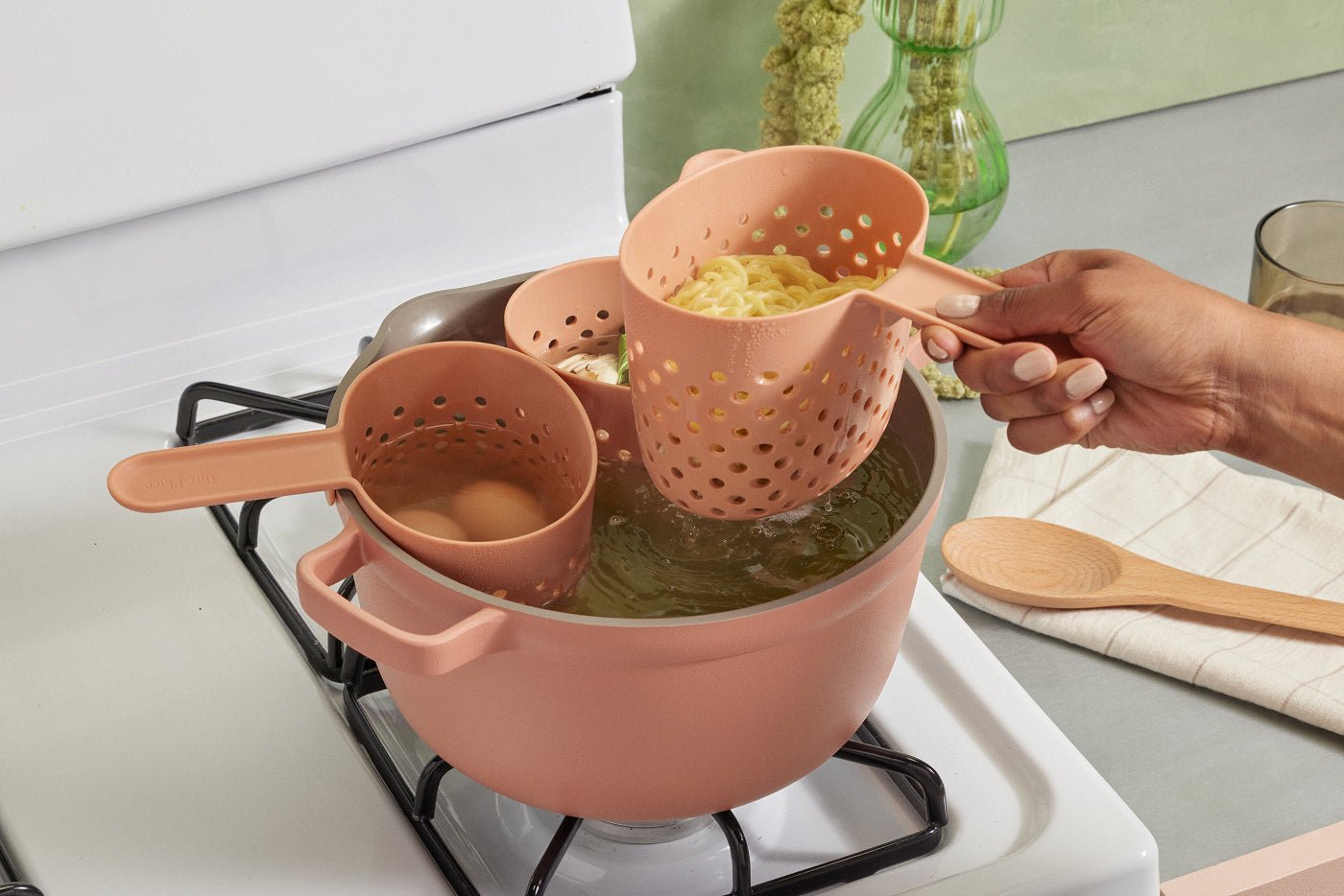 Three pink strainers in a pink pot on a stove