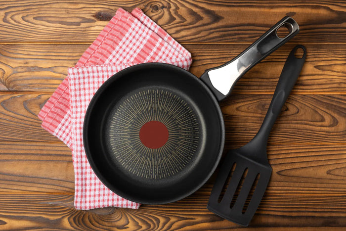 A nonstick pan and a black spatula on a wooden table