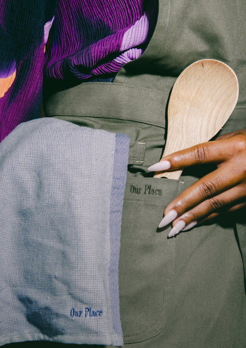 A chef wearing a green Home Cook Apron places a Beechwood Spoon in the pocket