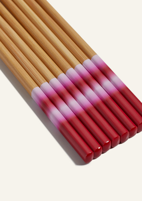 A set of wooden chopsticks with red and pink gradient tips, arranged side by side on a light background.