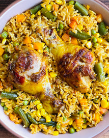 A plate of yellow rice mixed with peas, corn, green beans, and carrots, topped with two seasoned and cooked chicken drumsticks.