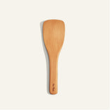 A wooden spatula with a flat, wide blade and a short handle, placed on a plain light background.