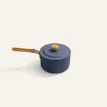 A blue saucepan with a matching lid and a wooden handle, placed on a light beige background.