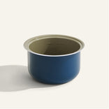 A blue, round, metal bowl with a light-colored interior, placed on a plain, light background.