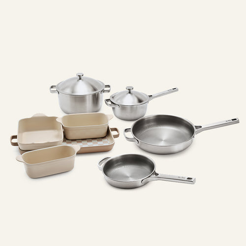 The Titanium Pro Cookware + Bakeware Set 2.0, consisting of stainless steel cookware and cream-colored ceramic bakeware.