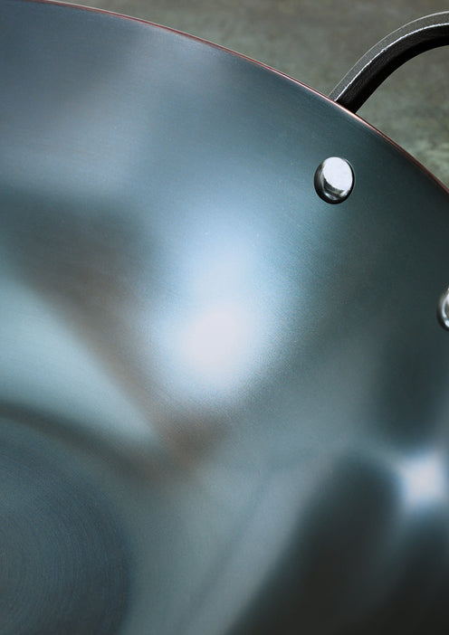 Close-up of a black wok with a metallic knob on a blurred background