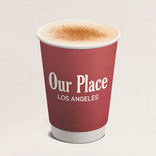 Red cup with 'Our Place Los Angeles' text and a cappuccino on a light beige background
