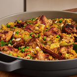 A close-up of a pan filled with chicken biryani, featuring rice, peas, spices, sliced almonds, and visible chunks of marinated chicken.