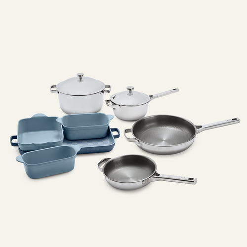 A Titanium Pro Cookware + Bakeware Set 2.0 featuring a collection of two lidded stainless steel pots, two frying pans, and blue ceramic bakeware.