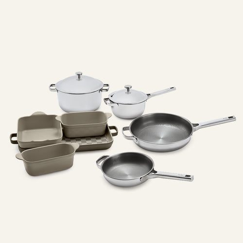 The Titanium Pro Cookware + Bakeware Set 2.0 includes stainless steel pots and pans with lids, alongside several rectangular, light brown ceramic bakeware dishes.
