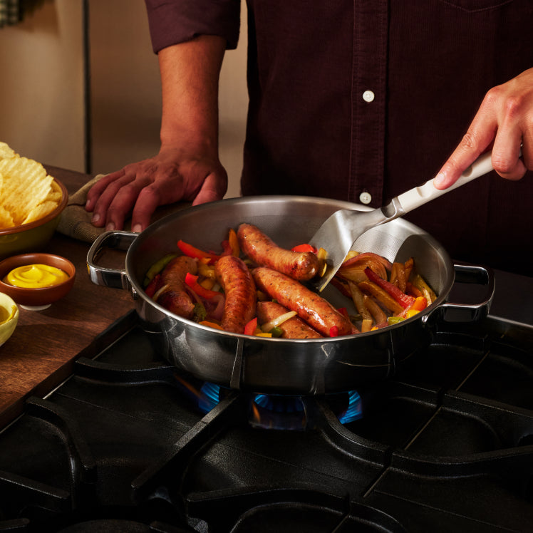 Sausages and peppers searing in a single layer across the wide base of the Titanium Braiser Pro.