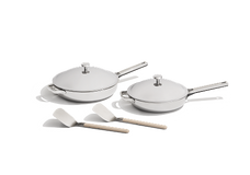 Two stainless steel frying pans with lids and two white spatulas with beige handles on a white background.