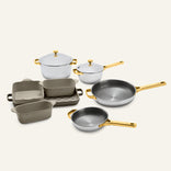 Titanium Pro Cookware + Bakeware Set 2.0 including two lidded pots, two frying pans, and three ceramic bakeware dishes with gold-toned handles and lids.