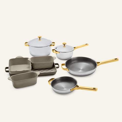 Titanium Pro Cookware + Bakeware Set 2.0 including two lidded pots, two frying pans, and three ceramic bakeware dishes with gold-toned handles and lids.