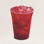 Red drink with ice in a clear plastic cup on a beige background