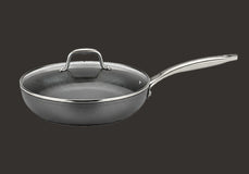 A nonstick frying pan with a glass lid and a long silver metal handle, displayed on a plain dark background.