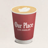 Red paper cup with 'Our Place Los Angeles' text and a cappuccino inside on a light beige background