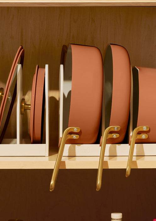 Set of brown cookware with gold handles on a wooden shelf.