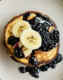 A stack of pancakes topped with sliced bananas and blueberry sauce, served on a light-colored plate.