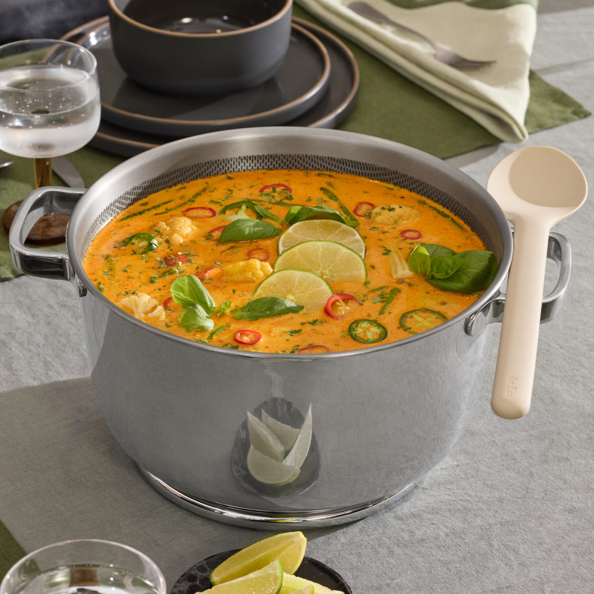 A Titanium Perfect Pot Pro filled with coconut curry soup, garnished with lime and basil.