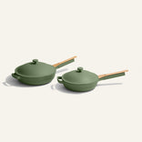 Two green nonstick pans with matching lids and wooden handles are displayed on a plain cream background. One pan is larger with a helper handle, while the other is smaller and more shallow.