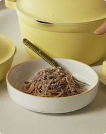 White bowl with spaghetti and a fork, yellow pot in the background
