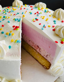 Ice cream cake with white frosting, colorful sprinkles, and a slice removed, on a white surface.