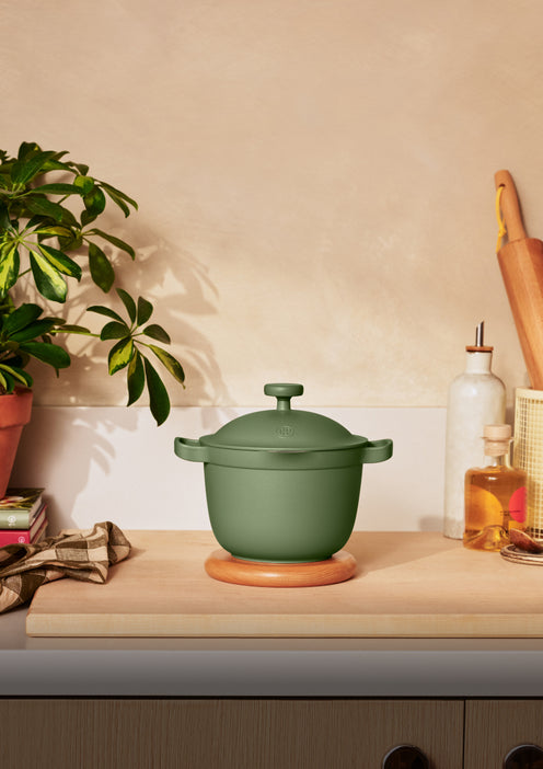 Green ceramic pot on a kitchen counter with a plant and kitchen items in the background.