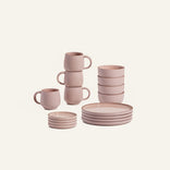 The Dinnerware Set features four pink ceramic bowls, mugs, and plates, all neatly arranged against a plain light background.