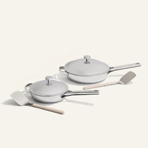 Set of white cookware with lids and wooden spatulas on a light gray background