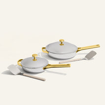 Set of white cookware with gold handles on a light beige background